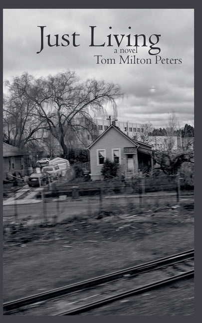Paperback book titled "Just Living" by Tom Milton Peters with a plain cover, resting on a wooden surface.